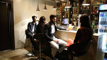A bar area with multiple stools, a refrigerator stocked with beverages, and a variety of bottles on shelves.