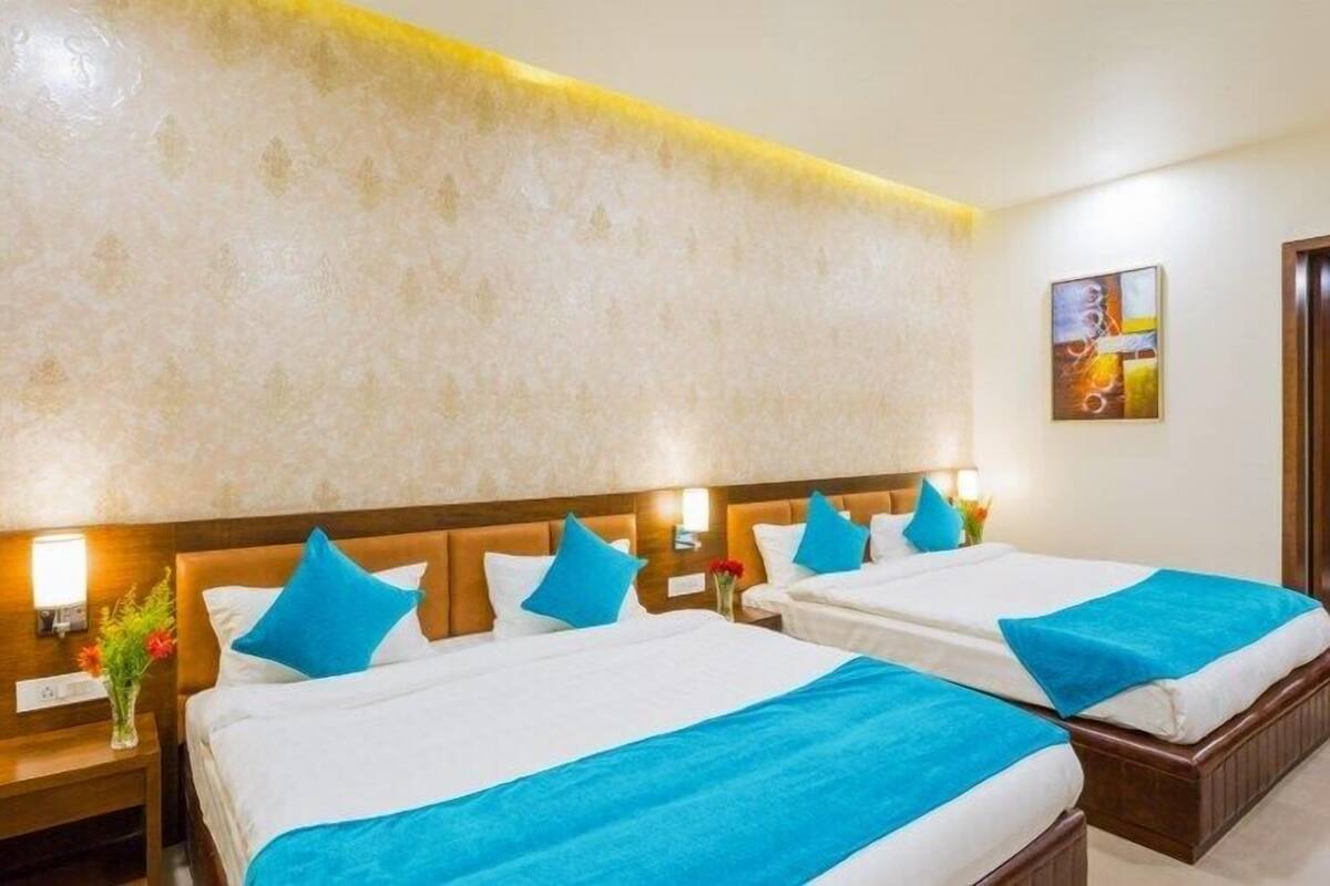 A hotel room with two beds, each with a blue bedspread and pillows, a wooden headboard, a nightstand with a vase of flowers, and a painting on the wall.