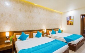 Une chambre d’hôtel avec deux lits, chacun recouvert d’une courtepointe bleue et agrémenté d’oreillers, une tête de lit en bois, une table de chevet avec un vase de fleurs et un tableau au mur.