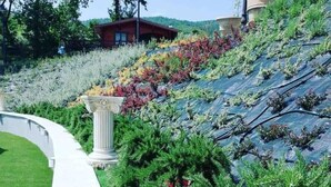 Ein angelegter Garten mit einem geschwungenen Weg, verschiedenen Pflanzen und einem Gebäude im Hintergrund.