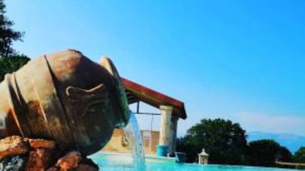 Ein Pool mit einem Wasserspiel, das an einen großen, schief stehenden Eimer erinnert, der Wasser in den Pool leitet.