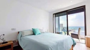 A bedroom with a bed, a nightstand, and a view of the ocean through large windows. - Sea View - Hassan II Mosque - By CasaPropreties (casablanca)