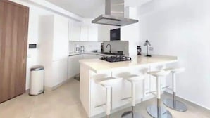 A modern kitchen with white cabinets, a stainless steel range hood, a built-in microwave, and a bar area with stools. - Sea View - Hassan II Mosque - By CasaPropreties (casablanca)