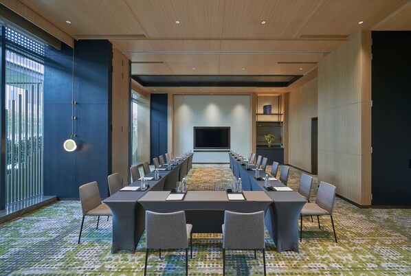 A conference room with a long table, chairs, and a large screen.