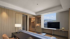 Une chambre d’hôtel moderne dotée d’un coin repas, d’un canapé, d’une télévision et offrant une vue sur le paysage urbain.
