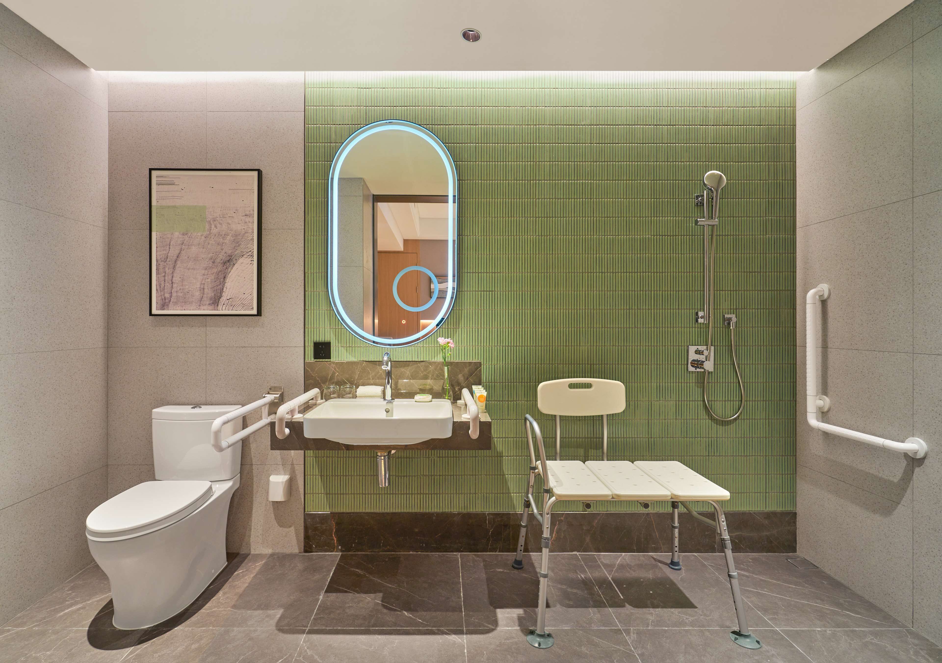 A modern bathroom with a toilet, sink, mirror, shower, and grab bars.