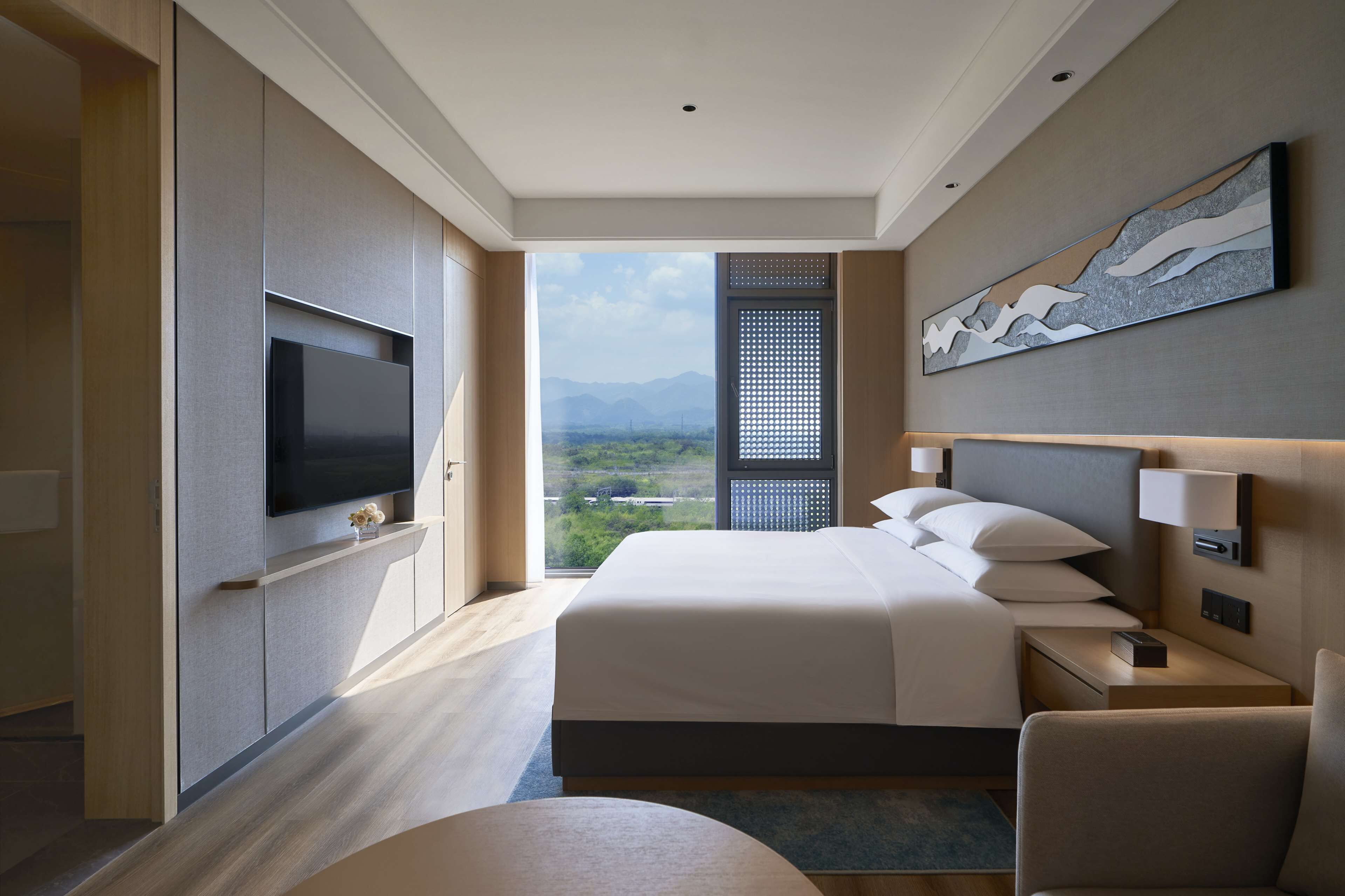 Ein modernes Hotelzimmer mit einem großen Bett, einem Flachbildfernseher, Blick auf die Berge und einem Bild an der Wand.
