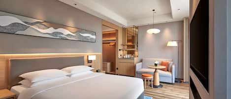 A hotel room with a large bed, a desk, a chair, a TV, and a kitchenette.