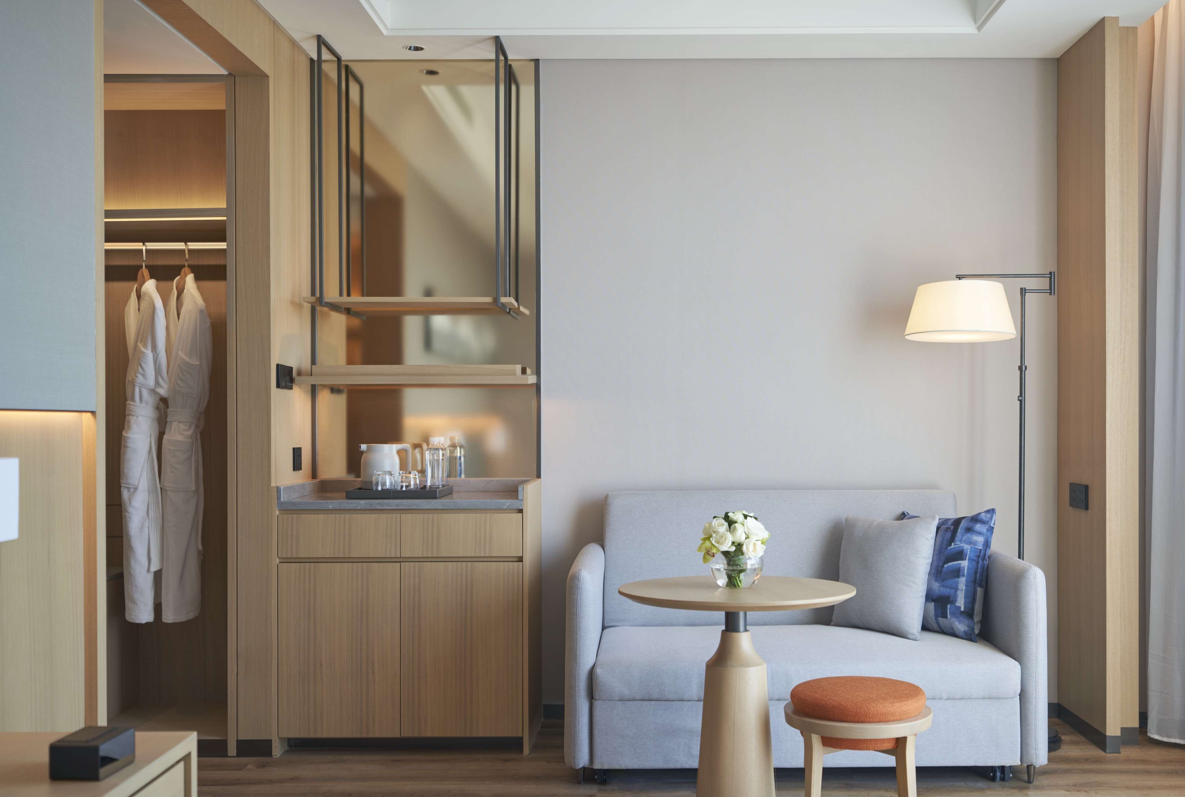 Une chambre d’hôtel moderne équipée d’une kitchenette, d’un canapé avec des coussins, d’une petite table ronde et d’un lampadaire.