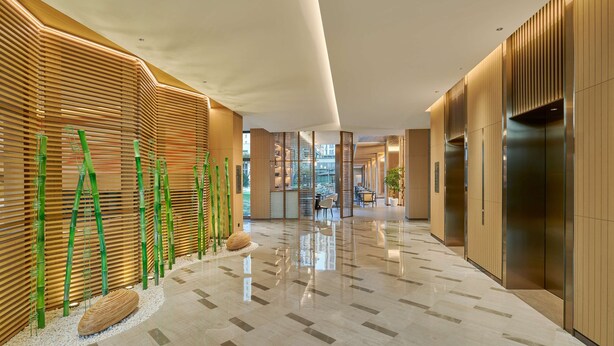 Un hall d’hôtel moderne avec un sol en marbre poli, des murs recouverts de lambris en bois et un espace de détente central agrémenté de tables et de chaises.