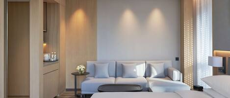 A modern hotel room with a large bed, a sofa, a small table with a vase of flowers, and a kitchenette area.