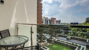 A balcony with a glass table and chairs, overlooking a landscaped garden and a cityscape. - The Tyrwhitt Unit 408 (Johannesburg)