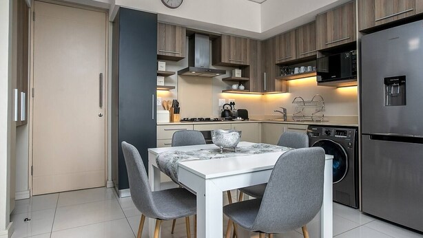 A modern kitchen with a dining table, chairs, a refrigerator, and a washing machine. - The Tyrwhitt Unit 408 (Johannesburg)