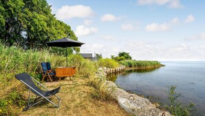 Een landschap aan het meer met een houten tafel en stoelen, een zwarte parasol en een stoel op het grasrijke strand.