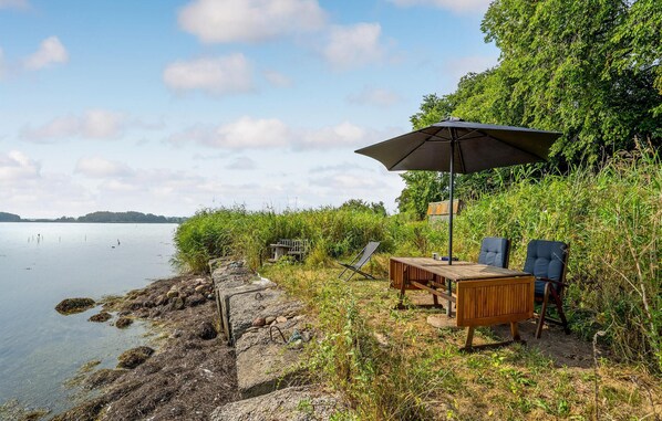 Een terras aan het meer met een tafel, stoelen en een parasol, met uitzicht op het water en heuvels in de verte.