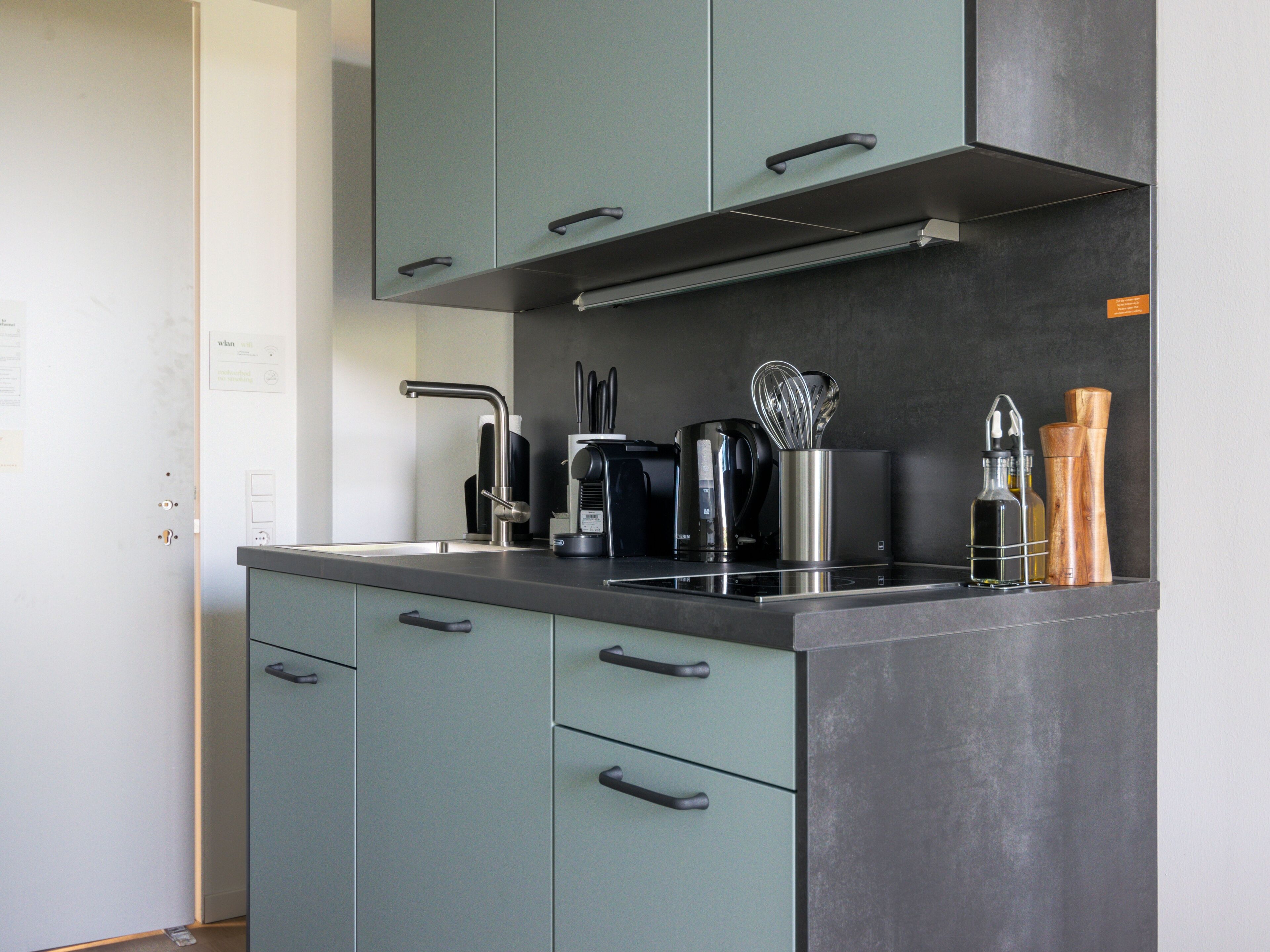 Una cocina moderna con un lavamanos de acero inoxidable, una cafetera y utensilios de madera sobre la encimera.