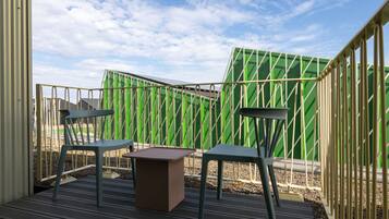 An outdoor seating area with two chairs and a table, surrounded by a green fence and a metal railing.