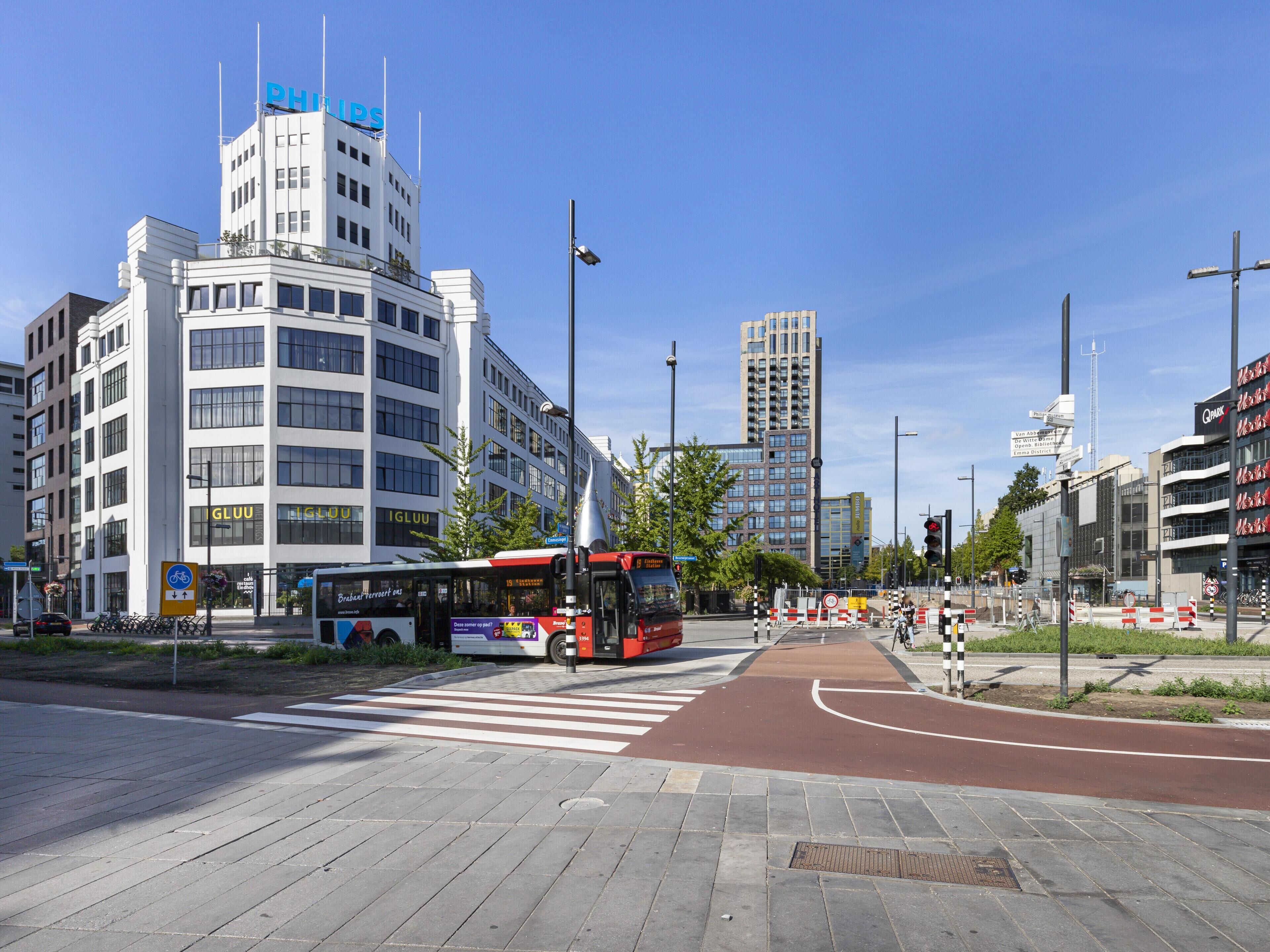 Una intersección urbana con un autobús rojo, edificios modernos y un paso de peatones.