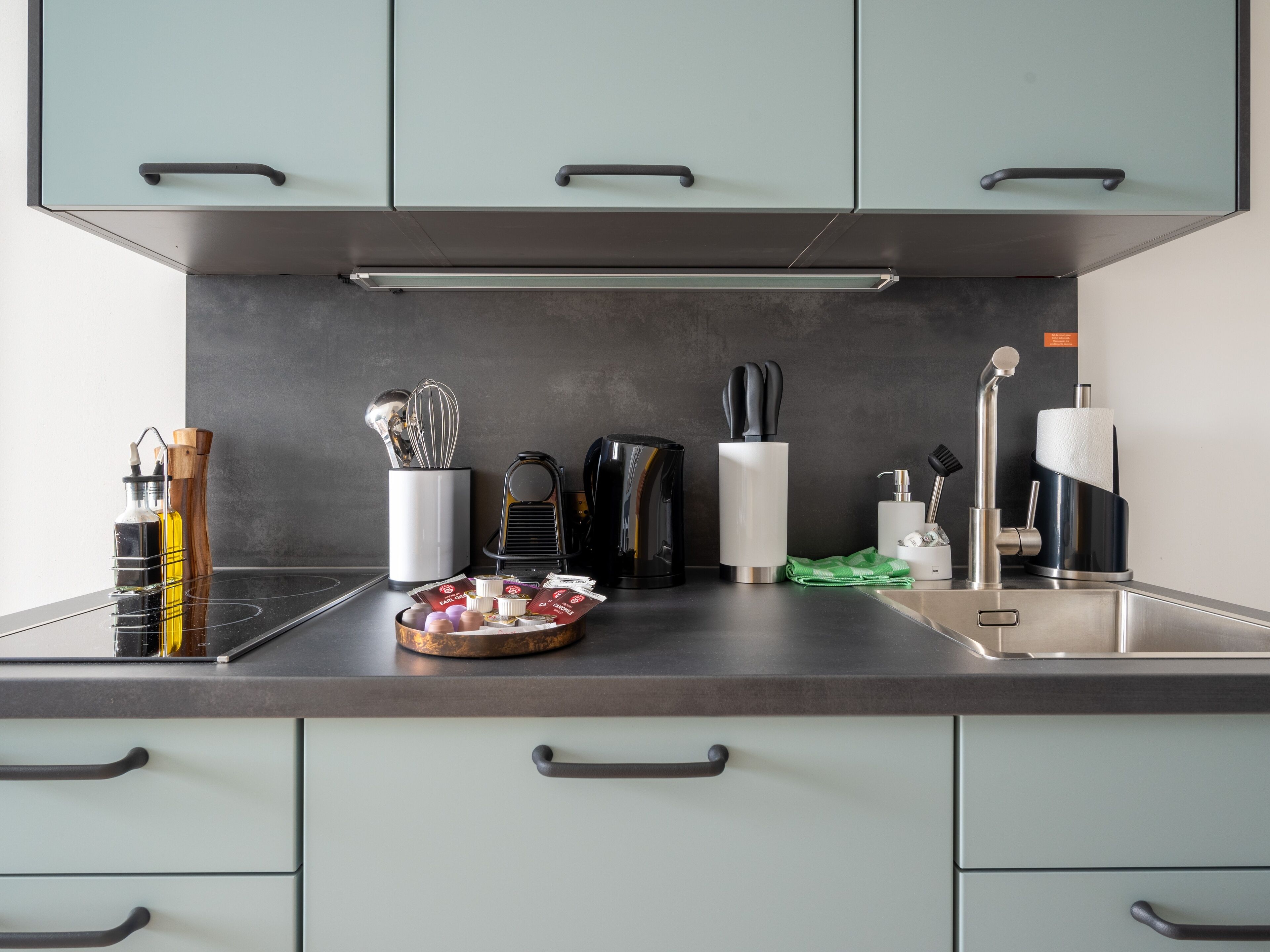 A modern kitchen with light green cabinets, stainless steel appliances, and a black countertop.