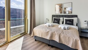 Une chambre d’hôtel moderne dotée d’un grand lit, offrant une vue sur la ville grâce à de larges fenêtres du sol au plafond, et disposant d’un balcon.