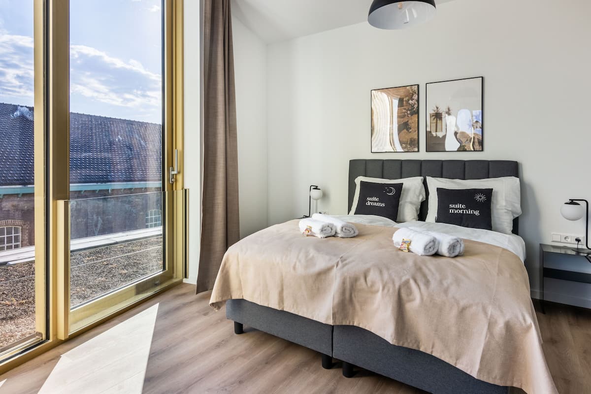 Een moderne hotelkamer met een groot bed, uitzicht op de stad door middel van kamerhoge ramen en een balkon.