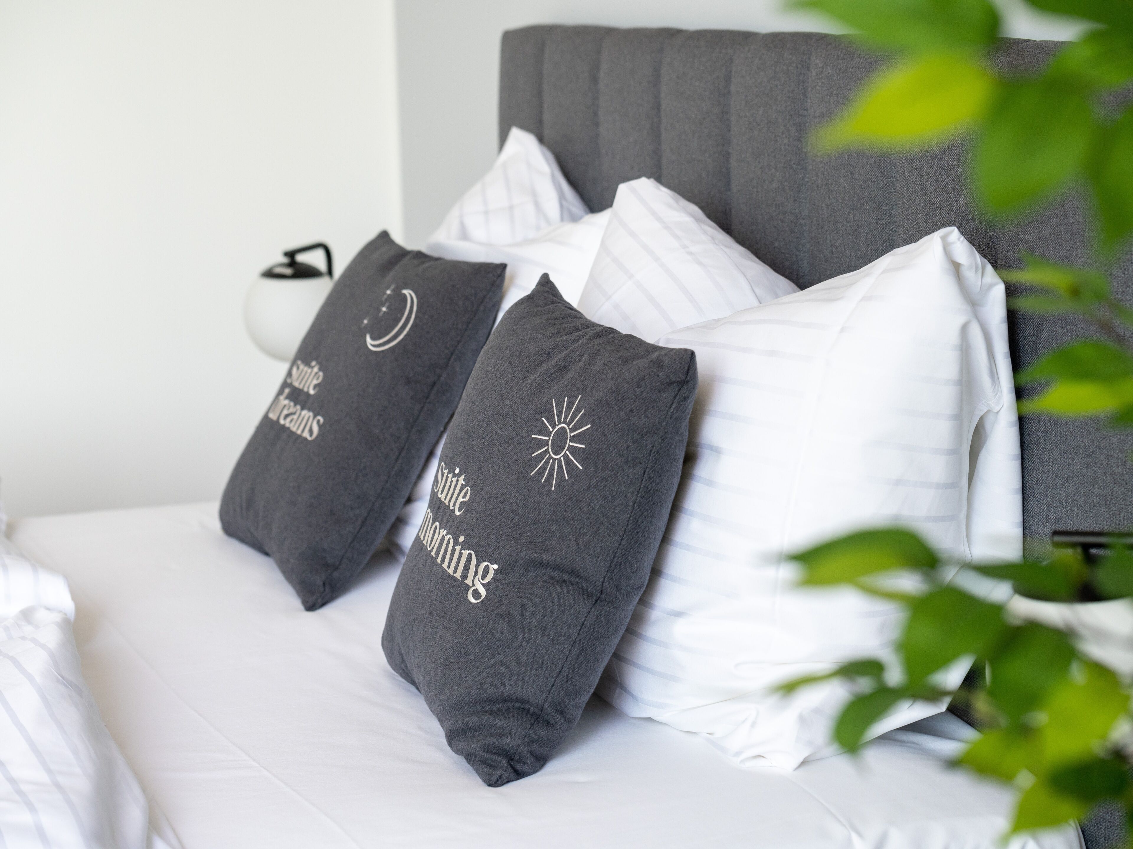 Een bed met witte beddengoed en twee grijze kussens met tekst en symbolen.