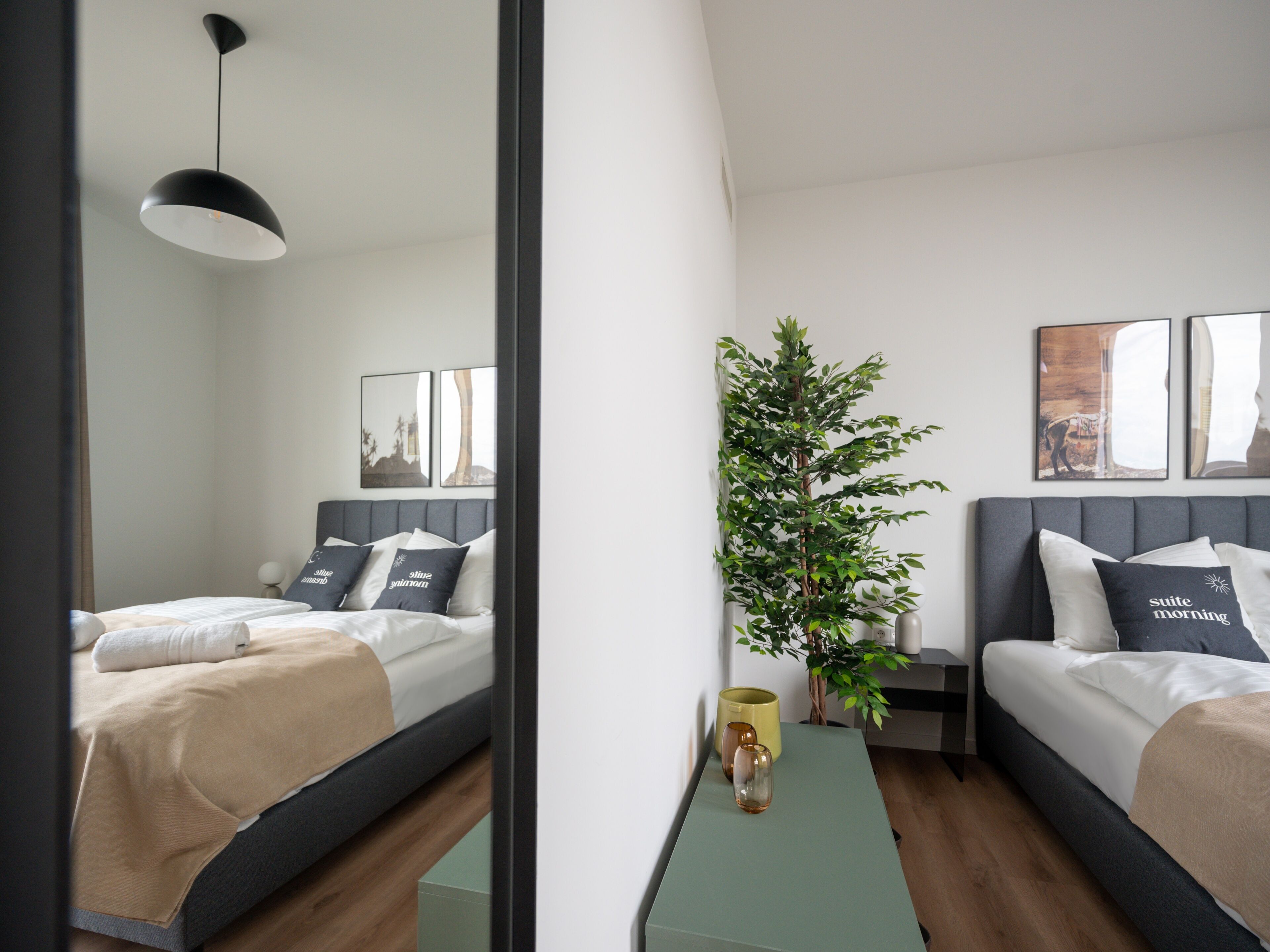 Une chambre d’hôtel moderne avec deux lits, une petite table, une plante en pot et des œuvres d’art accrochées aux murs.
