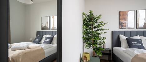 Une chambre d’hôtel moderne avec deux lits, une petite table, une plante en pot et des œuvres d’art accrochées aux murs.