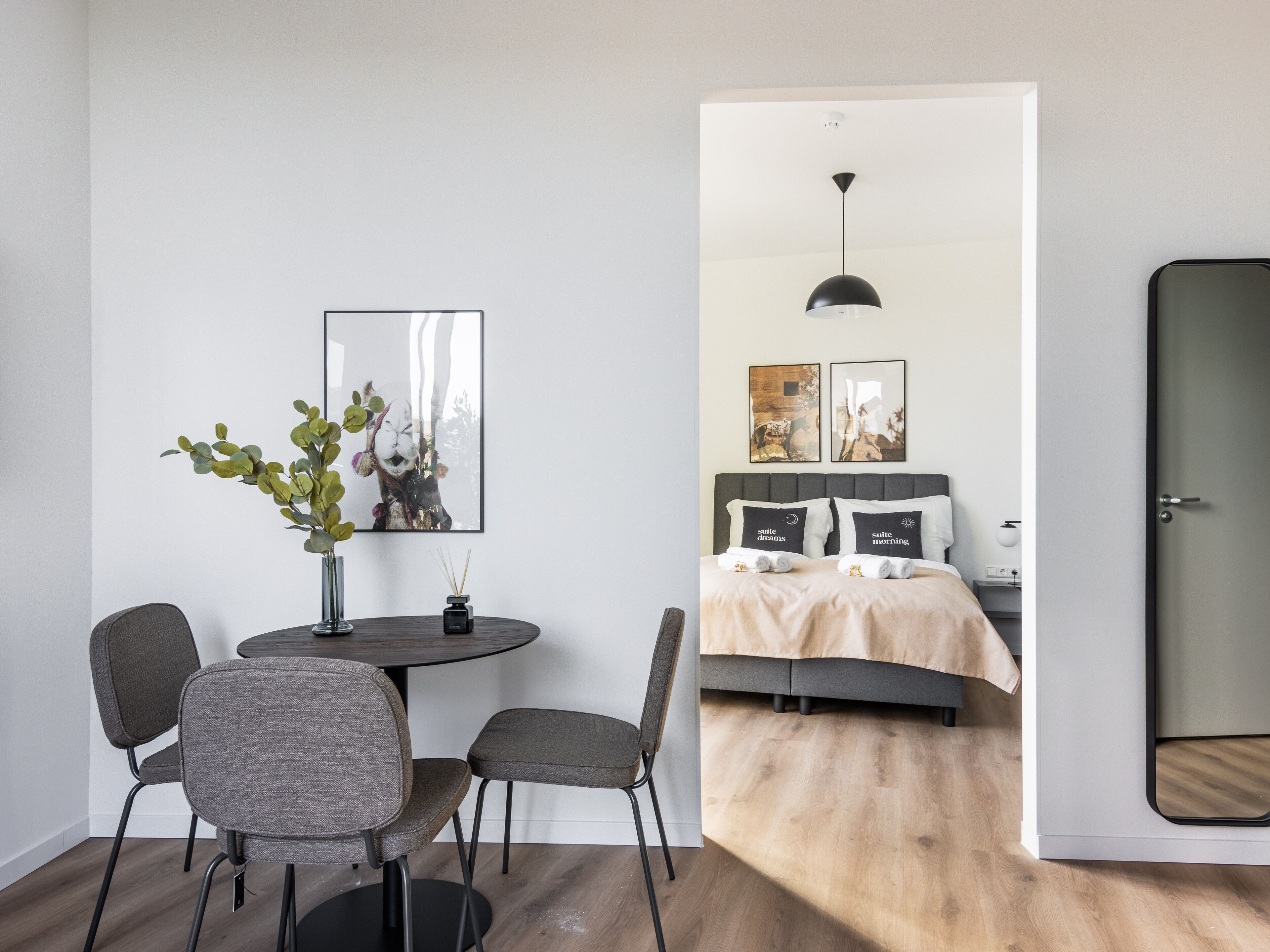 Una habitación de hotel moderna con cama, mesitas de noche y un comedor con sillas y una mesa.