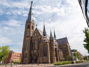 Une grande église en briques, dotée de nombreuses flèches et d’un haut clocher abritant une horloge.