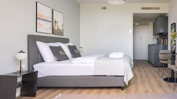 A modern hotel room with a large bed, bedside tables, a desk, and a kitchenette.