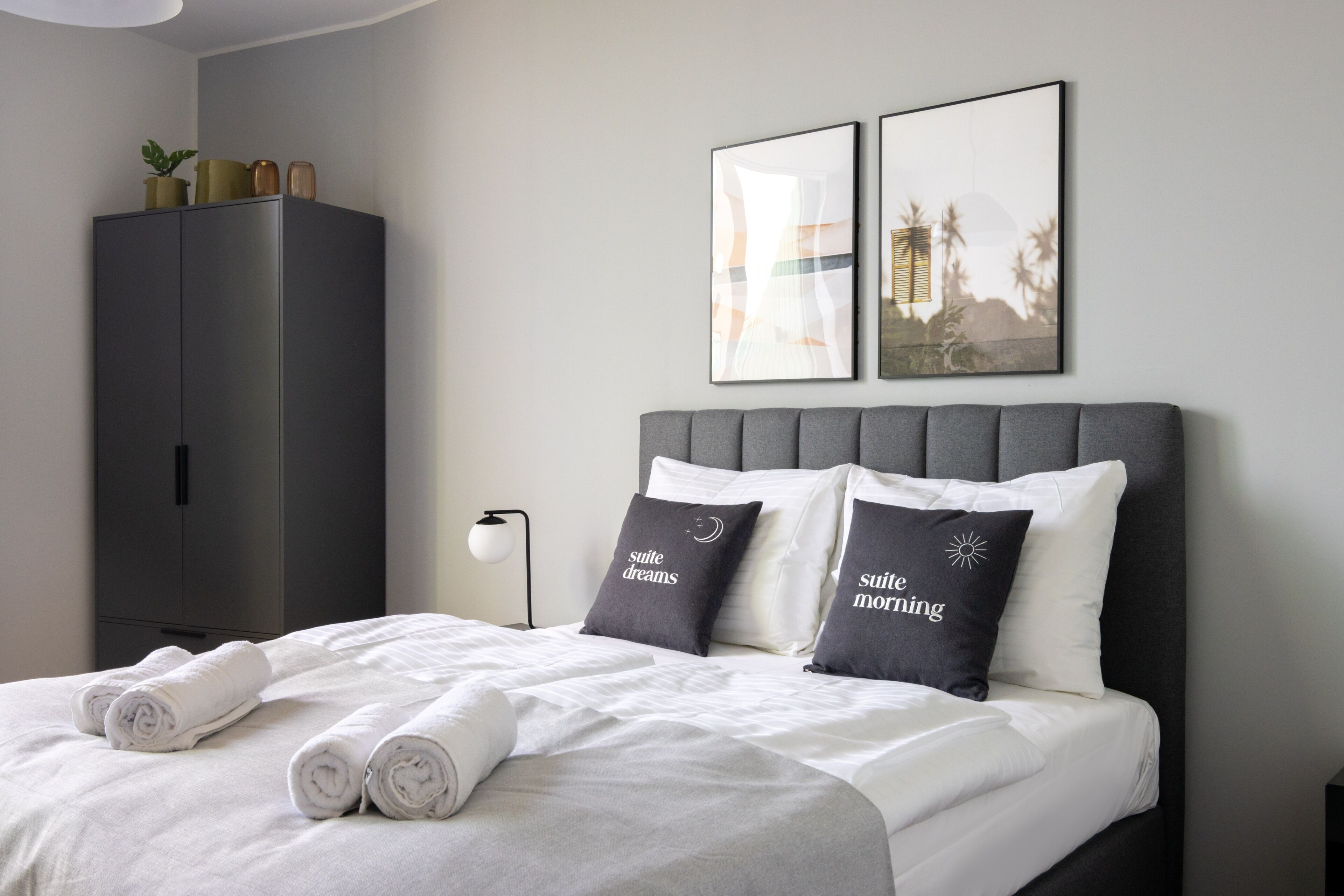 A neatly made bed with rolled towels, a grey headboard, and two pillows with text.