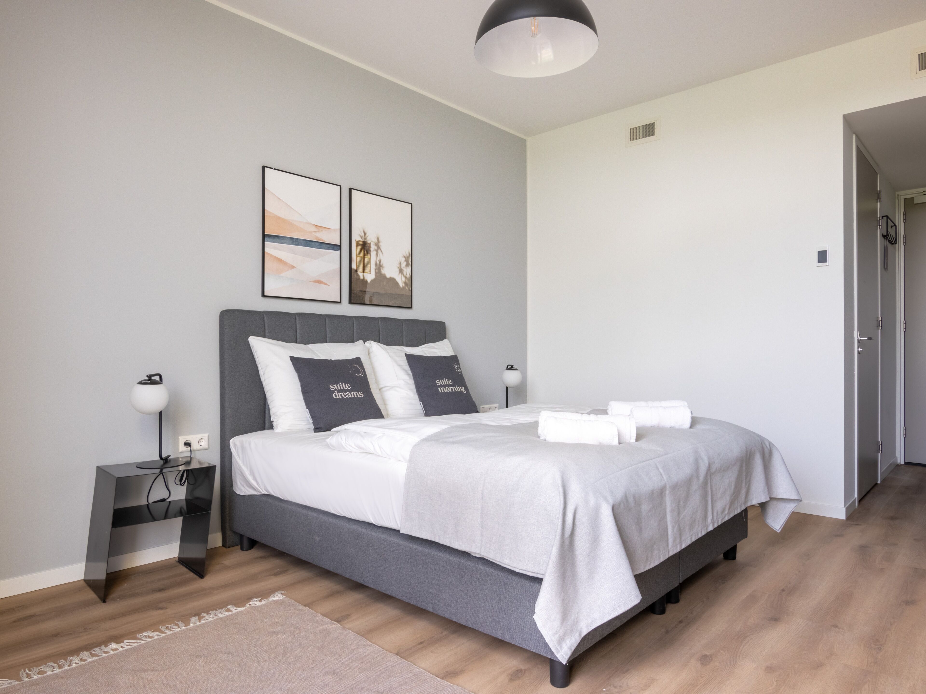 Un dormitorio moderno con una cama gris, ropa de cama blanca y dos cuadros en la pared.