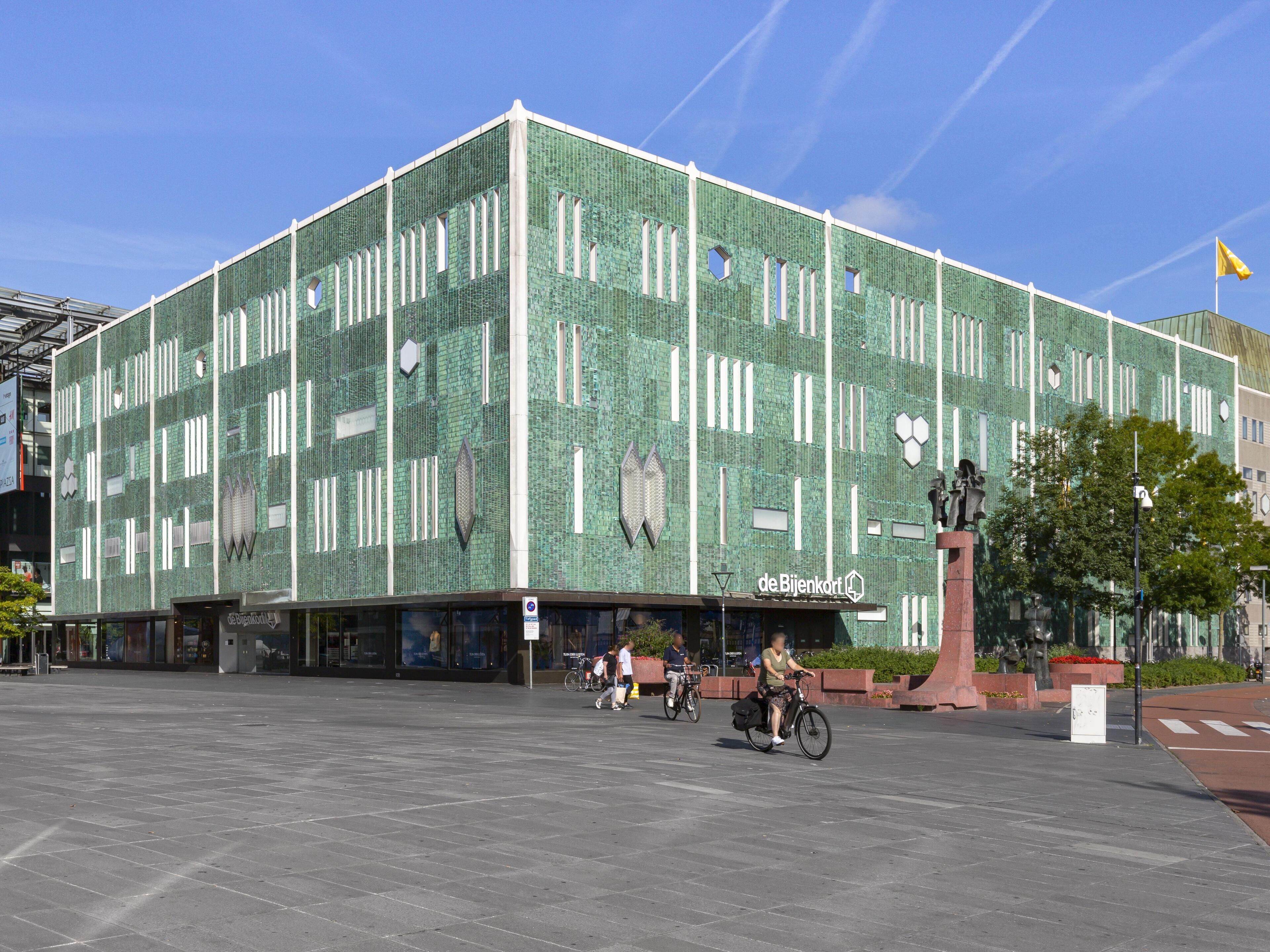 A modern building with a green mosaic facade, a statue in front, and a clear blue sky.