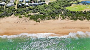 An aerial view of a coastal area with a sandy beach, a golf course, and a residential area with houses.