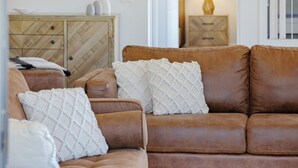 A brown leather sofa with white textured cushions in a living room.