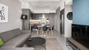 Ein modernes Wohnzimmer mit einem grauen Sofa, einem schwarzen Couchtisch und einem Fernseher auf einem Holzgestell.