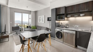 Eine moderne Küche mit Edelstahlgeräten, ein Essbereich mit Tisch und Stühlen sowie ein großes Fenster mit Blick auf die Stadt.