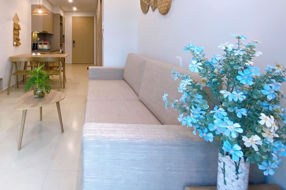 A modern living room with a flat-screen TV, wooden furniture, a dining area, and decorative plants.