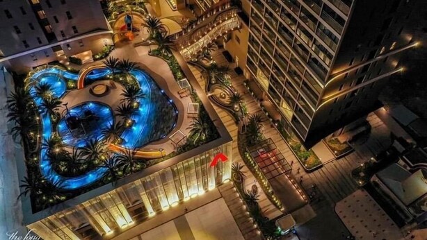 A high-rise hotel with a central swimming pool surrounded by palm trees and outdoor seating areas.