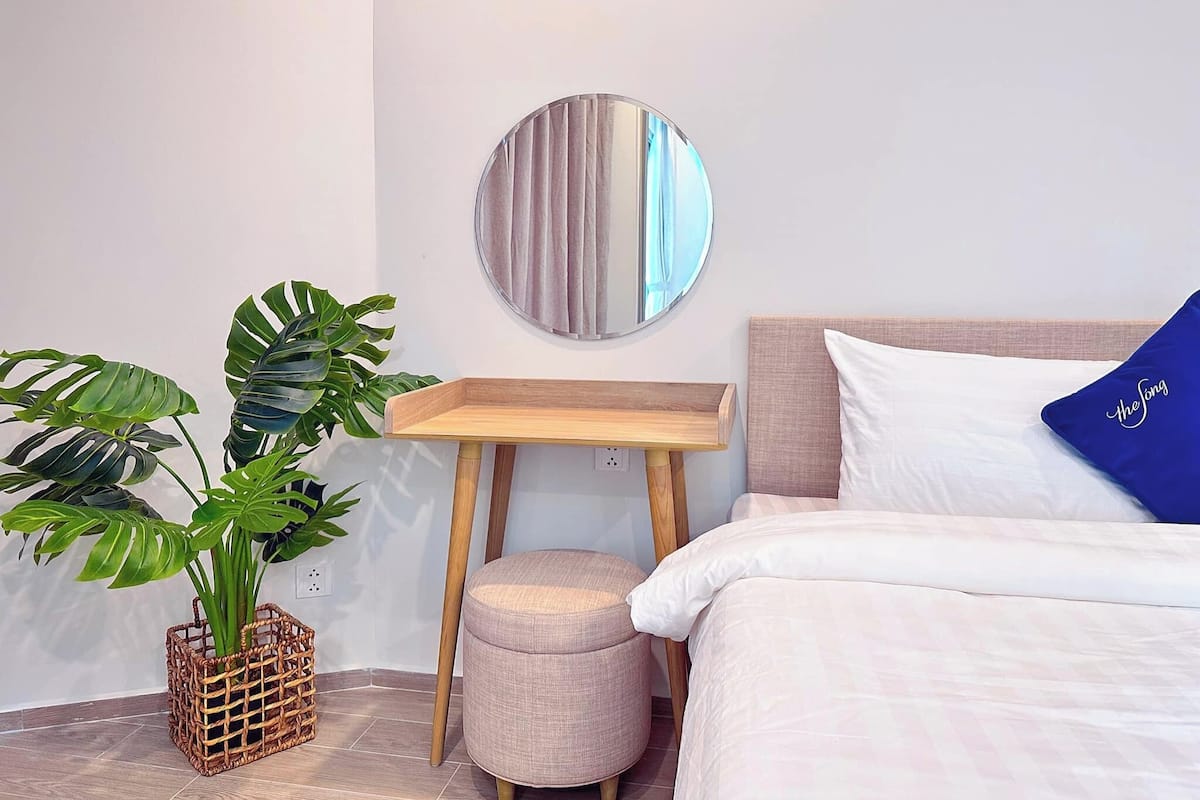A bedroom with a bed, a bedside table, a mirror, and a potted plant.