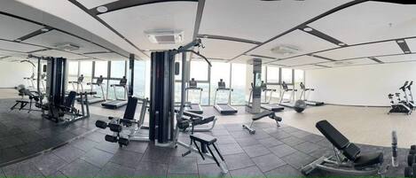 Un gimnasio con diversos equipos de ejercicio, amplias ventanas y un espacio amplio.