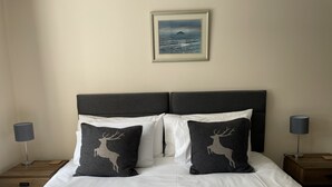 A neatly made bed with white bedding and two decorative pillows featuring a deer silhouette.