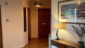 A hallway with wooden flooring, a console table with a lamp, a framed picture, and two hanging lamps.
