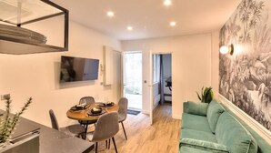 Una sala de estar moderna con un sofá verde, un comedor con una mesa redonda y sillas, y un televisor montado en la pared.
