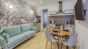 Una cocina moderna con comedor, que presenta un sofá azul claro, una mesa de madera con cuatro sillas y un televisor montado en la pared.