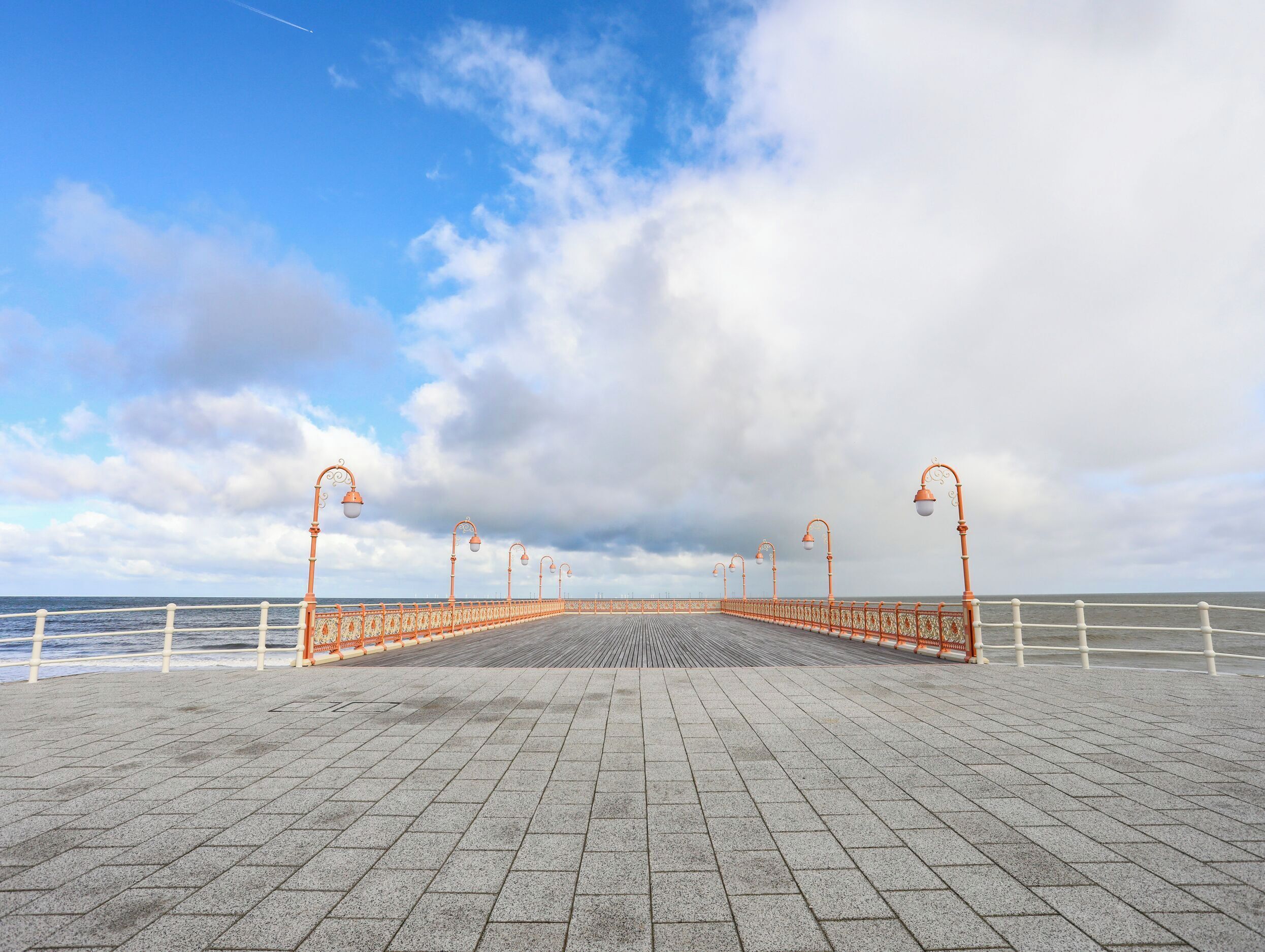 A paved promenade with a railing, street lamps, and a view of the sea.