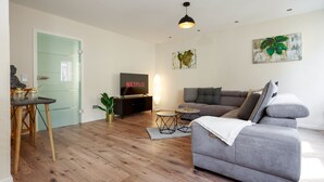 A modern living room with a grey sofa, a flat-screen TV, wooden flooring, and a green door. - Fewo für die Familie Dachterrasse Trocker/waschmaschine Netflix Jarody (Senheim (Mosel))