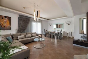 A modern living room with a sectional sofa, a glass coffee table, and a dining area with a chandelier.