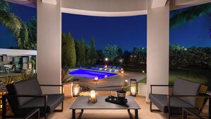 Ein Poolbereich mit Sitzgelegenheiten im Freien, einem Tisch mit Kerzen und Blick auf ein Schwimmbad bei Nacht.